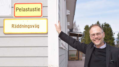 Jukka Pietinen vid modulskolan i Sjundeå. På skolväggen n skylt där det står "räddningsväg" på både finska och svenska.