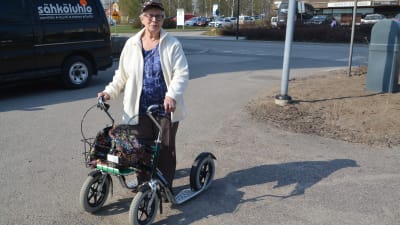 Dam med rollator står i solen på en asfalterad väg
