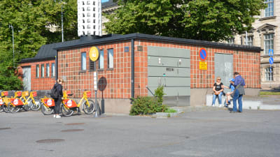en av åbo stads offentliga toaletter. den här vid ån nära ukko-pekka, en orangebrun tegelbyggnad med fölicyklar bredvid sig.