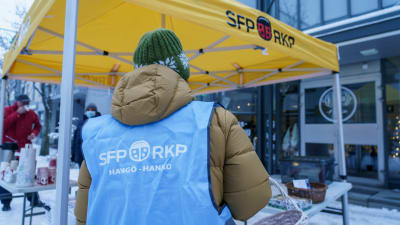RKP:n liiviin pukeutunut henkilö RKP:n vaaliteltan edessä. Selässä lukee SFP RKP Hangö Hanko.