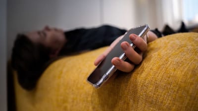 Anonyymi nainen makaa vuoteellaan puhelin kädessään.