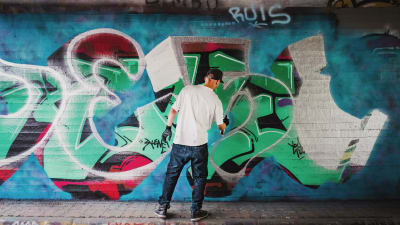 Janne Saarikoski gör graffitikonst. En färggrann vägg där det står hans graffitialias DESI.
