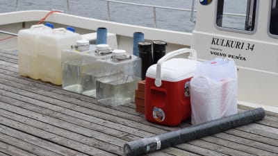 plastdunkar, gummistövlar, matbox med mera på en brygga som väntar på att lastas in i en båt.