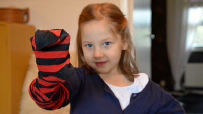 Flicka med röd-svartrandig strumpa på handen.