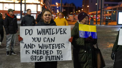 En kvinna med en skylt som det står "do whatever you can and whatever is needed to stop Putin"