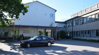 RAseborgs sjukhus, huvudingången fotograferad utifrån. En svart bil står perkerad utanför dörren. Sommar. 