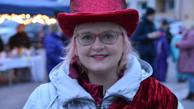 Kvinna i röd sammatshatt står och ler.