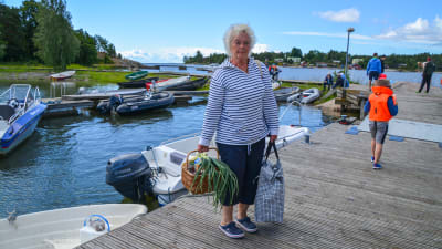 En kvinna står med en korg och en väska på en brygga.