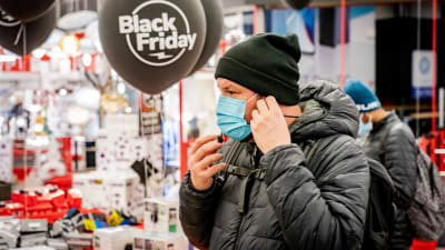 En person i ansiktsmask vid ingången till en butik under Black Friday.