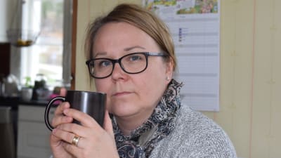Christel Lindqvist-Jauhiainen sitter i sitt kök med kaffemugg i handen. Allvarlig, ler inte.