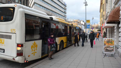 En dam med lila jacka stiger av en vitgul buss i Åbo centrum.