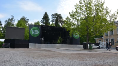 En konsertscen på en grusplan med ett träd i förgrunden.