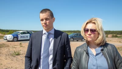 Den ledande polisduon i första säsongen av Kaikki synnit stående framför en polisbil.