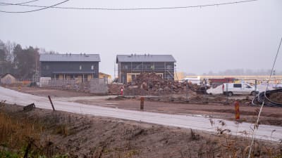 Byggarbetsplats med två nästan färdiga hus vid väg. 