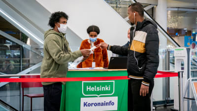 En mörkhyad man tar emot ett munskydd vid Helsingfors corona-informationspunkt i ett köpcentrum.