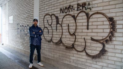 En man står invid en graffitimålning i en portgång.