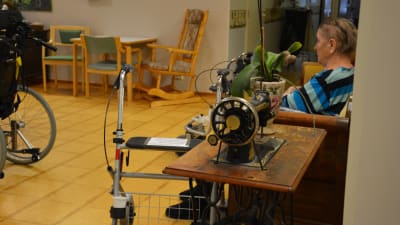 Gammal symaskin i förgrunden, rollator och äldre person i bakgrunden.