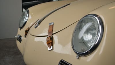 Framdelen på en beige Porsche 356. Runda lampor, två bruna läderbälten som håller fast motorhuven.