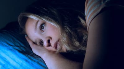 Nuori nainen pää tyynyllä selaa kännykkää unettomana.