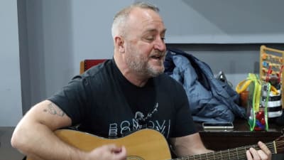 En skäggig man i 50-årsåldern spelar gitarr.