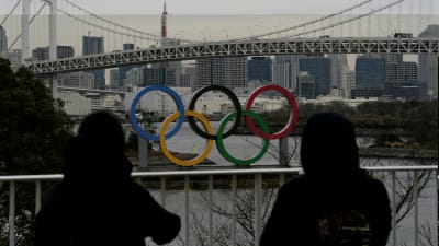Två personer står och tittar på de olympiska ringarna i Tokyo