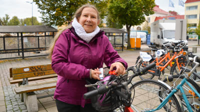 En kvinna som står bredvid sin cykel och visar upp två cykellyktor.