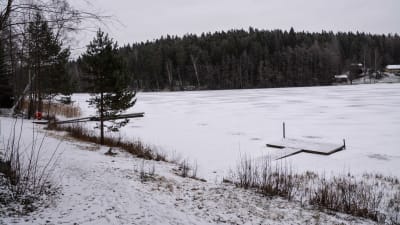 En snötäckt strand vid en istäckt sjö. Till vänster en rak träbrygga och till höger en t-formad träbrygga som har sjunkit ner lite vid bryggfästet.
