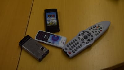 Några icke riktiga mobiltelefoner (leksaker) och en fjärrkontroll till tv på ett bord.