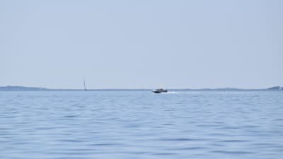 En motorbåt på ett lugnt, klarblått hav en sommardag. Segelbåtar långt i fjärran.