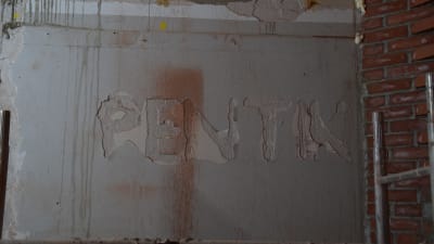 En murad vägg inne i ett stenhus där man kan se resterna av firmanamnet Pentik.