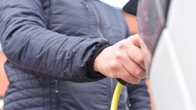 En person i blå jacka kopplar i en laddningskabel i en vit elbil.
