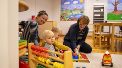 Två vuxna damer och två barn leker i lekrum.