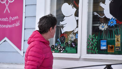 Kvinna tittar in i ett skyltfönster med muminfigurer på.