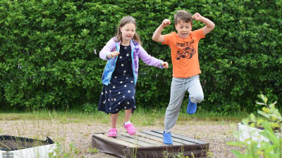 Maija och Erik Sallegren hoppar i en trädgård. 