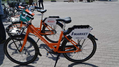 Två orange cyklar står på ett torg.