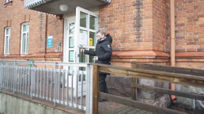 En ramp leder upp till en dörr i ett tegelhus, en kvinna håller upp dörren