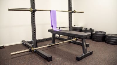 En bänkpress står i ett rum ämnat för träning. Vid sidan om ligger en mängd vikter på golvet.