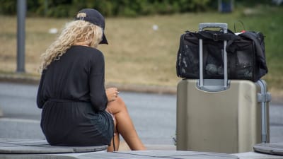 Kvinna sitter och tittar på sin telefon med kappsäck bredvid sig.