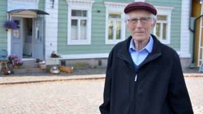 Äldre man med lila keps poserar vid Rådhustorget i Borgå.