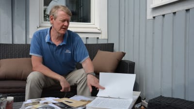 Kaj Mattsson sitter på verandan och bläddrar i en släktforskningsmapp.