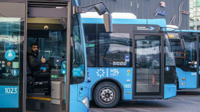 Busschaufför i en av HRT:s blåa bussar sitter parkerad med öppen dörr.
