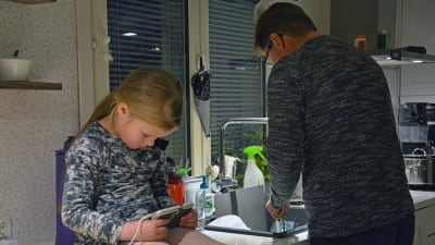 En flicka spelar på telefonen, i bakgrunden diskar en man.
