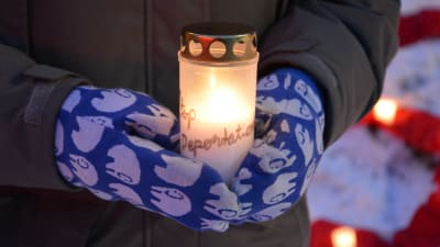 En person håller i ett levande ljus under en demonstration. 