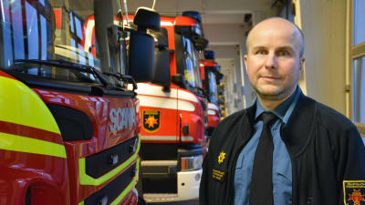 Vit man står framför rad av brandbilar.