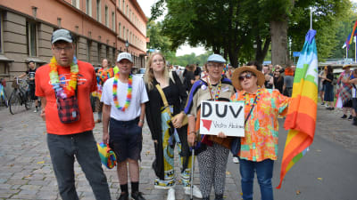 Fem personer i färggranna kläder, regnsbågsflagga och skylten DUV Västra Åboland tittar in i kameran.