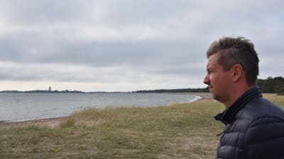 Man klädd i mörkblå jacka blickar ut över en strand.