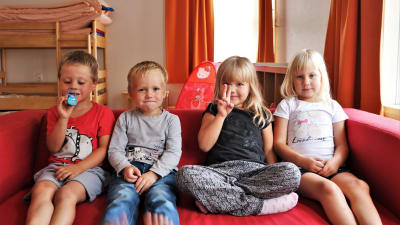 Barnen Kevin, Noel, Saga och Veronica sitter i en röd soffa, tittar in i kameran och ler.