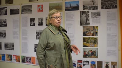 En kvinna vid en vägg med stora affischer med text. Utställning om bibliotekets historia i Hangö.