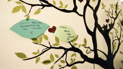 Två handskrivna lappar uppklistrade på ett målat träd på en vägg. På lapparna står det: "Don't believe everything you think" och "storms don't last forever".