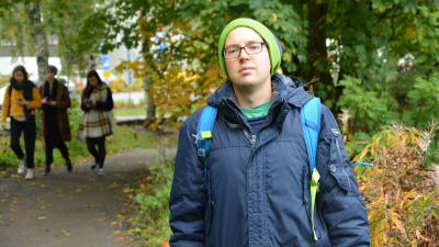 en kille i mörkblå jacka står vid en grönskande stig i ett parkområde i åbo